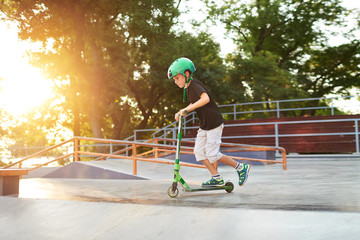 A boy on a scooter and in protective helmet do incredible stunts in skate park. Extreme jump. The...