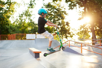 A boy on a scooter and in protective helmet do incredible stunts in skate park. Extreme jump. The...