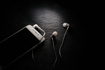 White smartphone and headphones on black background