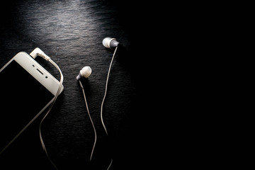 White smartphone and headphones on black background