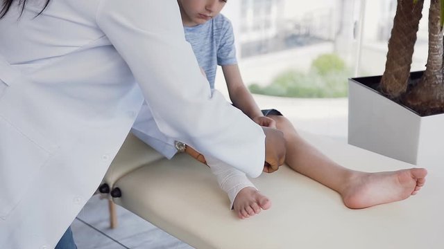 Female doctor hands bandaging leg of cute boy.