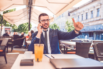 Handsome business man in glasses talking by mobile phone showing thumbs up