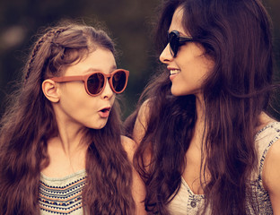 Happy fashion mother talking with her excited daughter in trendy sunglasses on nature summer background. Closeup