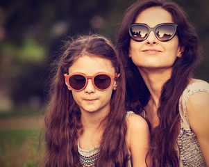 Happy fashion mother embracing and her daughter in trendy sunglasses on nature summer background. Closeup toned color