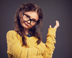Thinking angry kid girl gesticulating the hand in eyeglasses on grey studio background. Closeup...