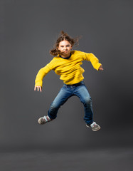 Funny happy child girl jumping in casual blue jeans and yellow pullover on grey studio background