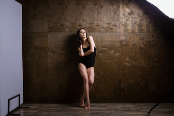 Baskstage, photoshoot from the side Beautiful young sexy woman with long flowing hair poses in photo studio on a shaved wooden background in black lingerie, swimsuit. In the studio light frame