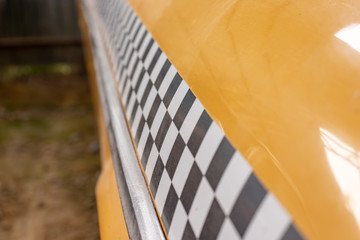 Checkered taxi sign on a yellow taxi car doors close up