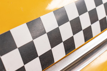 Checkered taxi sign on a yellow taxi car doors close up