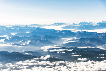 Naklejka na ściany i meble Landscape aerial view of colorful blue Alps mountains with clouds and fog above Switzerland