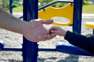 Baby daughters hand in daddy's hand at playground