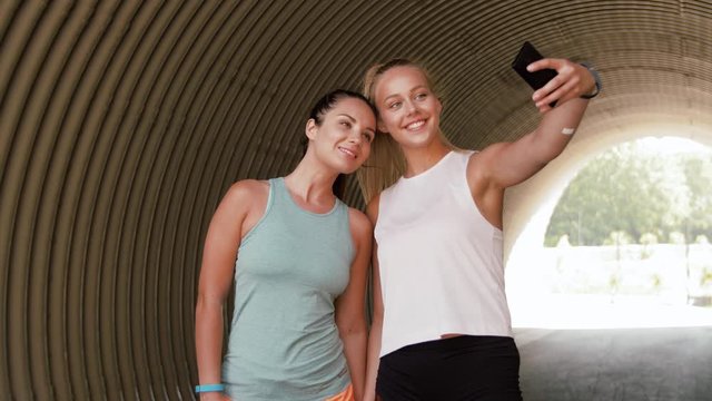 fitness, sport and healthy lifestyle concept - smiling young women or female friends taking selfie by smartphone outdoors