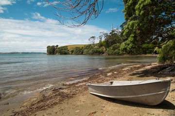 Algies Bay on Matakana coast near Snells Beach. Sunny day after a storm. Seaweed and debris washed up on shore. Clouds in sky, summers day. Small row boat, dingy in foreground on shore. Perfect beach.