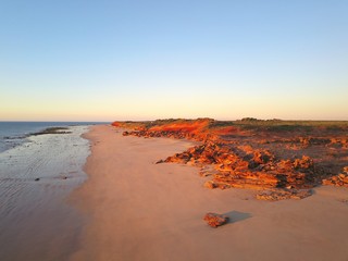 Scenic aerial panoramic view of remote coast near Broome, Western Australia, with ocean, beach, red cliffs, outback landscape and sunset blue sky as copy space.
