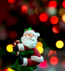 Santa Claus de adorno sujeto a la punta de árbol de navidad, en un fondo difuso de luces de colores.