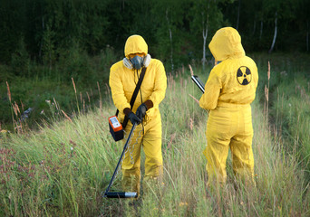 Two dosimetrist  in protective suite and mask with geiger counter measuring radiation level in danger zone - obrazy, fototapety, plakaty