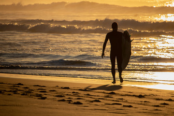 Surfer walking observing the surf on a beach at sunrise