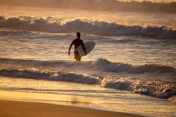Surfer entering the surf at a beach during sunrise or sunset