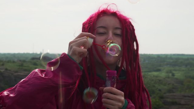 Beautiful girl with pink dreadlocks blowing soap bubbles to the camera footage