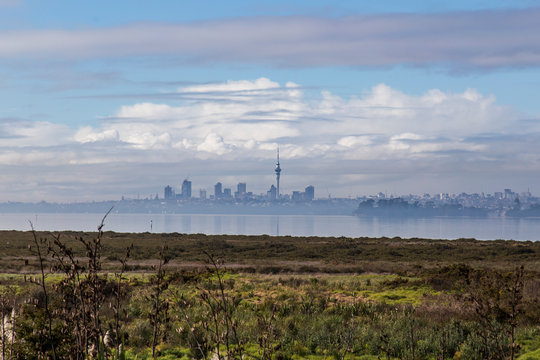 Auckland city scape from Te Atatu, West Auckland. Looking out to sky tower and surrounding buildings across the harbour and marshes, wetlands. Water is still, reflections, misty with clouds brewing.
