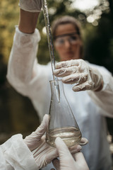 Scientists biologists and researchers in protective suits taking water samples from polluted river.