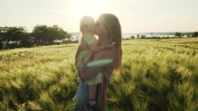 Mother hold baby girl and kiss her in the wheat field sunset rapid slow motion