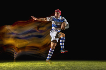 Caught in important moment. One caucasian man playing rugby on the stadium in mixed light. Fit young male player in motion or action during sport game. Concept of movement, sport, healthy lifestyle.