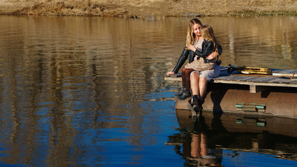 Fashionable stylish family for a walk. Mom and daughter sits on a wooden pier near the lake....