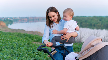 Young caring mother on walk with two children. Eldest child in her arms sits in her mother arms,...