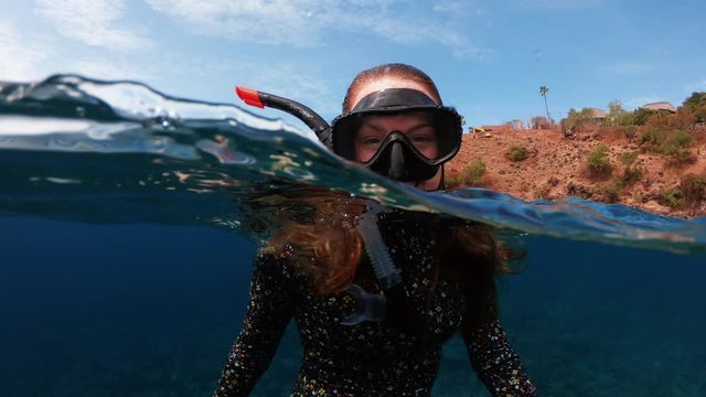 Happy Snorkelling Girl Waving to Camera Underwater in Tropical Destination with Coral Reef Below, 50-50 dome split slow motion