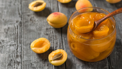 Apricot jam with a wooden spoon in a glass jar on the table.
