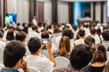 Rear view of Audience listening Speakers and using mobile phone taking the picture in the...