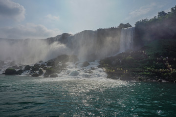 Niagara Falls, NY: Tourists in yellow raincoats at the Cave of the Winds, stairs and platforms at the foot of the Bridal Veil Falls, on Goat Island.