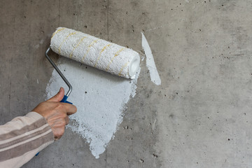 A painter paints a concrete wall with white paint, a male hand with a paint roller for painting a...