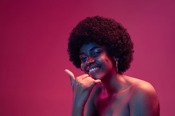 Summer's sunset. Portrait of female fashion model in neon light on pink gradient studio background. Beautiful african woman with trendy make-up and well-kept skin. Vivid style, beauty concept.