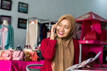 Fototapeta na wymiar portrait of a young muslim entrepeneur sitting and smile talking in her smartphone in front of fashion boutique as background -image