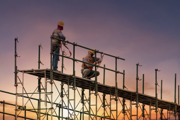 Man working on construction site with scaffold and building with sunset background,scaffolding for construction factory - obrazy, fototapety, plakaty