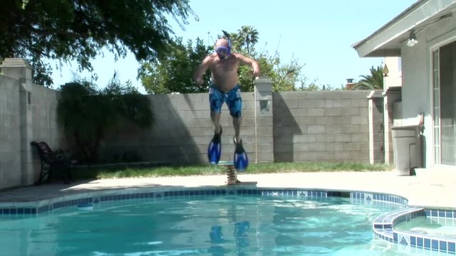 A man wearing fins and a snorkel jumps off of a diving board into a pool.