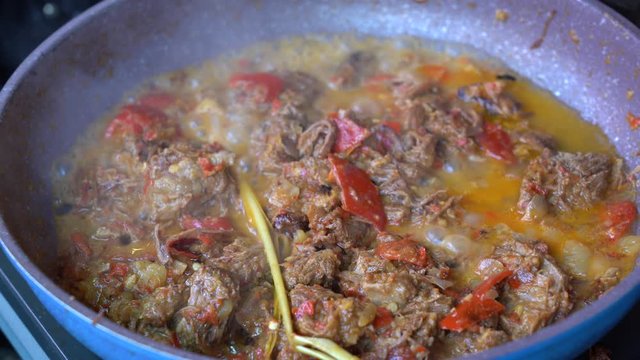 Frying pan with onion, lemongrass, red pepper and beef meat, close up. Indonesia. Sambal Goreng Ati Kentang, Indonesian cuisine, spicy beef meet and potatoes garnish with lemongrass leaf and red chili