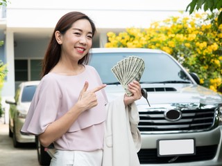 Asian woman holding money and car key against a car. insurance, loan and finance concept