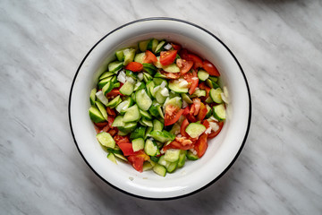 Tomatoes, fresh cucumbers and onion salad. The salad in a plate on the table. Chopped and mixed vegetables. Eco friendly products. Top view