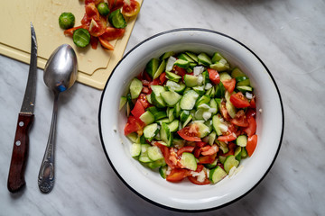 Tomatoes, fresh cucumbers and onion salad. The salad in a plate on the table. Chopped and mixed vegetables. Eco friendly products. Knife and spoon near to the plate on the cutting board. Top view