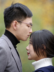 Portrait of a handsome Chinese young man kissing his beautiful girlfriend's forehead, romantic couple relationship, side view with blur nature background.