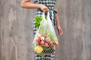 Female hand with cotton eco bag on wooden grey background. Zero waste concept
