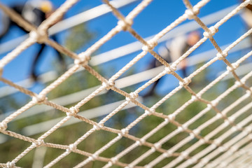 White mesh close-up. A blurry person overcomes an obstacle In the background. Sport event. Clear blue sky