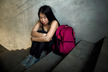 Dramatic portrait of Asian female college student bullied. Young depressed and sad Korean girl sitting lonely on campus staircase suffering bullying and harassment