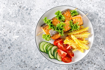 Grilled salmon kebab on skewers with baked potato, fresh cucumbers and tomatoes
