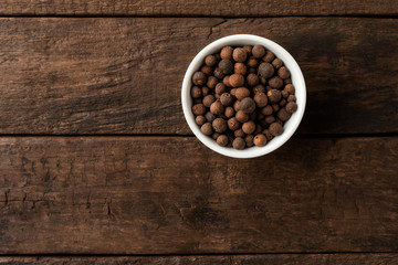 Allspice in bowl on retro wooden background. Top view