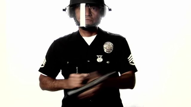 A police officer in riot gear swipes a baton back and forth.