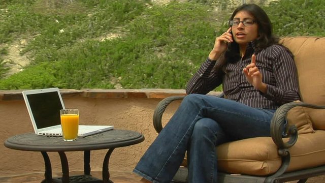 A woman speaks into a cell phone while sitting on a patio.